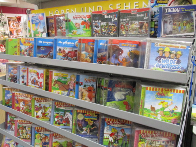 In einem Regal stehen mehrere Reihen bunter Kinder-Audio-CDs und DVDs mit Zeichentrickfiguren und beliebten deutschen Serien wie Die drei ???, TKKG und Bibi & Tina.