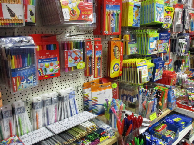 Eine Auslage mit verschiedenen Schreibwaren wie Buntstiften, Markern, Kugelschreibern, Buntstiften und Zeichensätzen, die in einem Geschäft ordentlich in Regalen und an Haken aufgehängt sind.