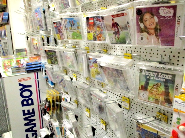 Eine Auslage im Kaufhaus Heitmüller zeigt Reihen von Nintendo 3DS-Spielehüllen in durchsichtigen Plastikhüllen an einer Stellwand, daneben ein Schild mit der Aufschrift GAME BOY. Einige Hüllen mit Animations- und Zeichentrickfiguren sind zu sehen.