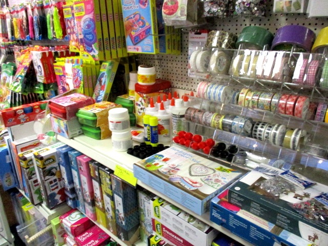 In einem Regal im Kaufhaus Heitmüller in Wennigsen sind die Bastelutensilien - Klebeflaschen, Farben, bunte Bänder, Schleifen und Bastelsets - übersichtlich und hell angeordnet.