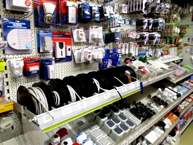 In einer Auslage bei Haus&Co Fachgeschaeft in Wennigsen ist Elektronikzubehör wie Kabel, Steckdosenleisten, Adapter und Batterien übersichtlich auf Regalen und Stecktafeln angeordnet.