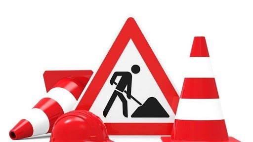 Ein Baustellen-Warnschild mit einer Person, die gräbt, umgeben von zwei orangefarbenen Verkehrskegeln und einem orangefarbenen Bauhelm, alles auf weißem Hintergrund - perfekt für Ihr nächstes Haus&Co-Projekt in Wennigsen oder im Kaufhaus Heitmueller.